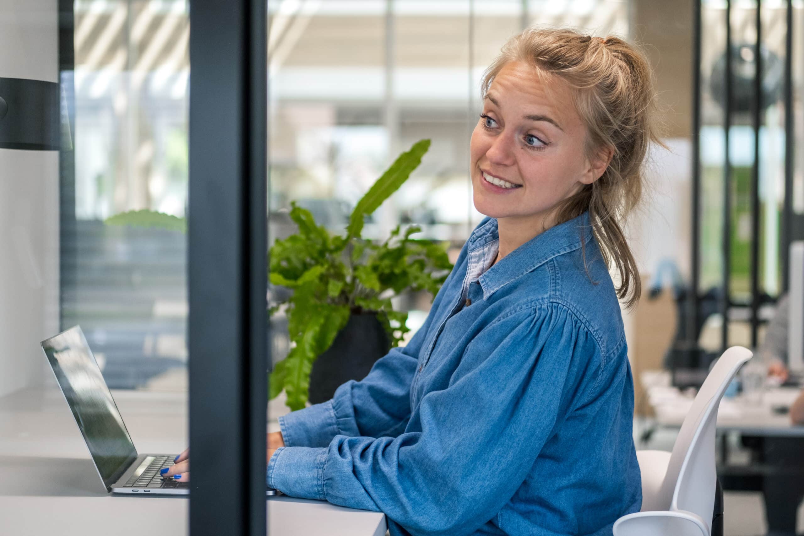 Lachende jonge vrouw zittend aan een bureau in een modern kantoor